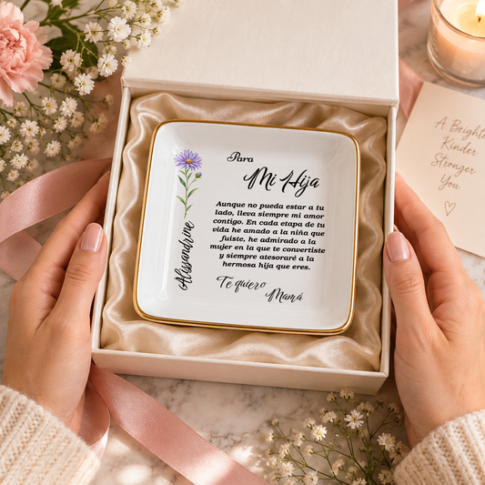 Manos sosteniendo una caja de regalo abierta que contiene un plato de joyeria personalizado con una flor morada y el mensaje en espanol Para Mi Hija.